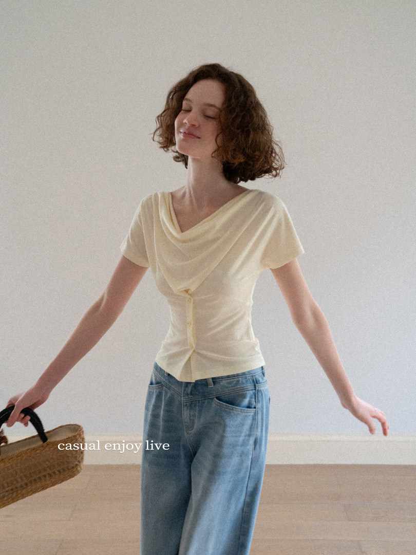 Model wearing a cream draped short-sleeve top with blue jeans