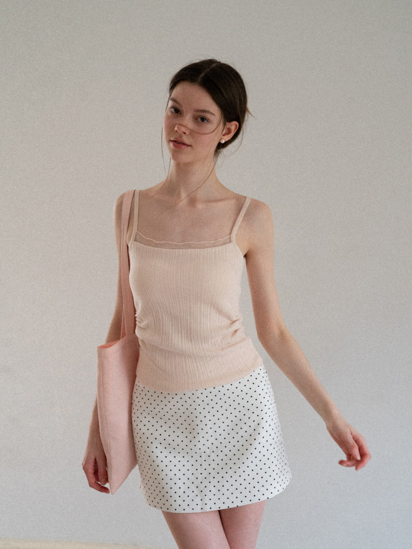 Model wearing a beige camisole top and white polka dot mini skirt
