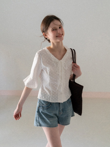 Woman modeling a white blouse with denim shorts and a black shoulder bag