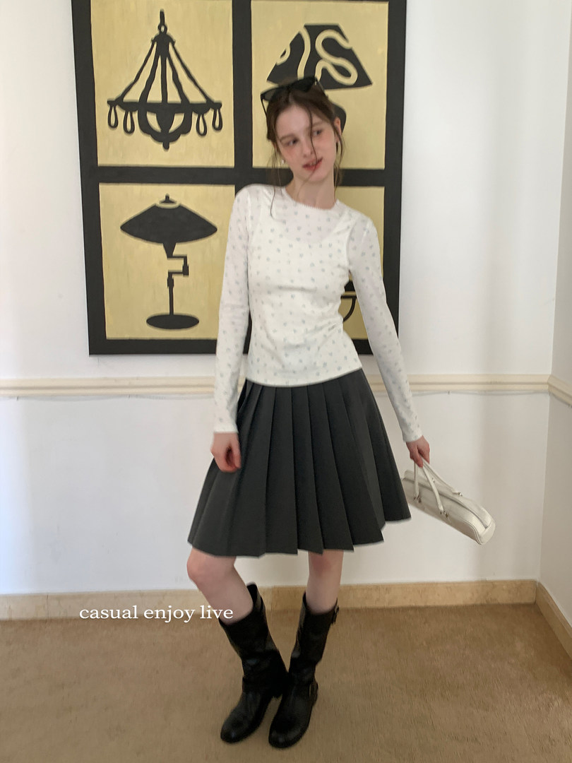 Woman modeling a white long-sleeve top with a black pleated skirt and black boots