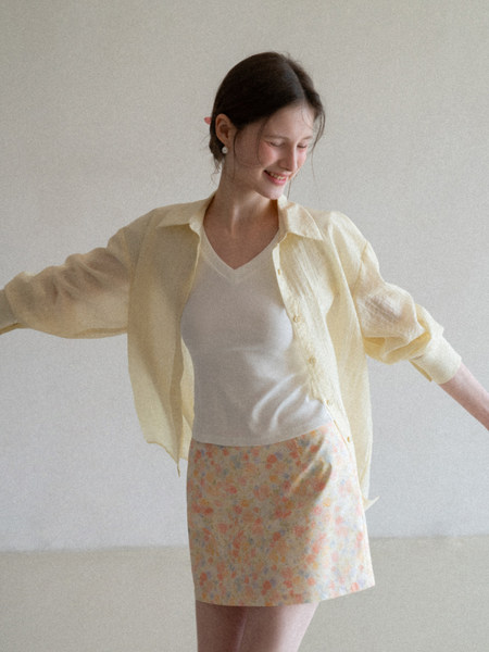 Model wearing a sheer pale yellow button-up shirt over a white top with a floral mini skirt