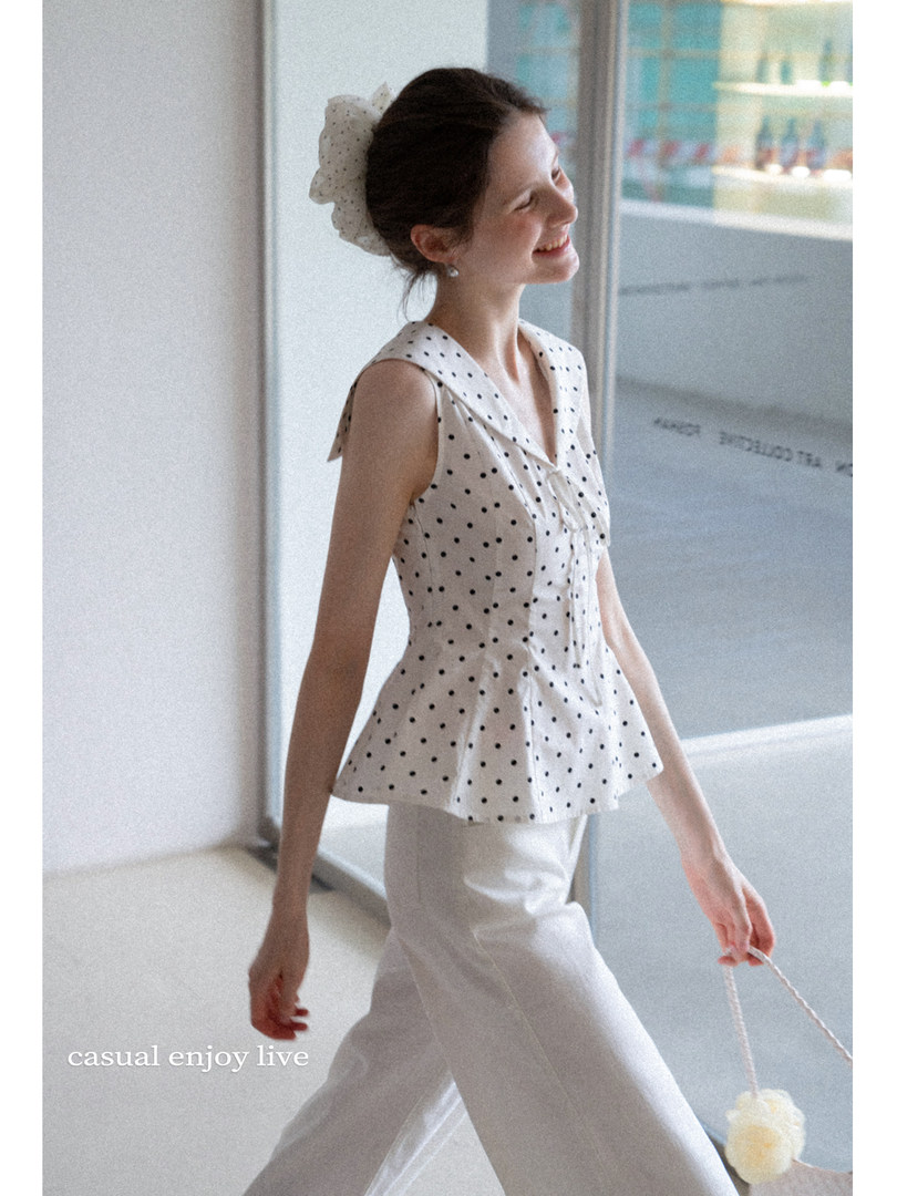 Model wearing a white sleeveless polka dot top with white pants