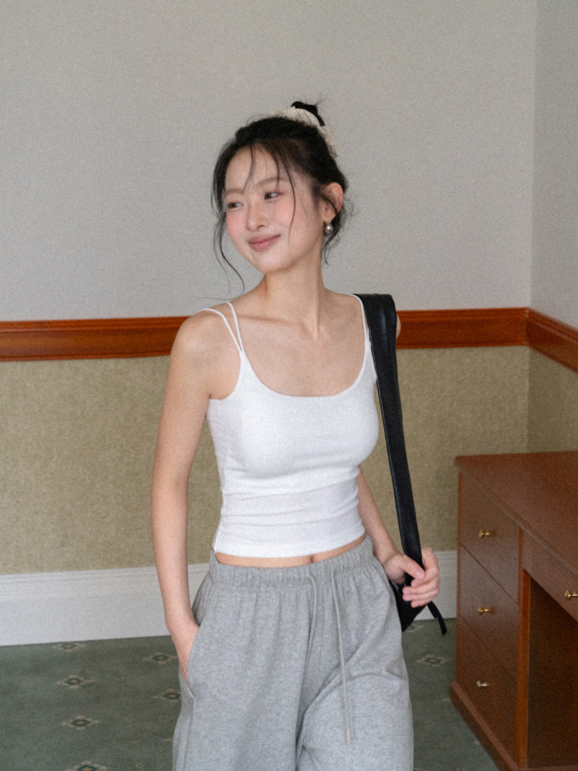 Woman wearing a white spaghetti-strap tank top and gray loose pants