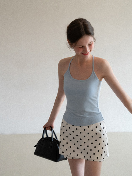 Woman wearing a light blue tank top and polka dot skirt holding a black handbag