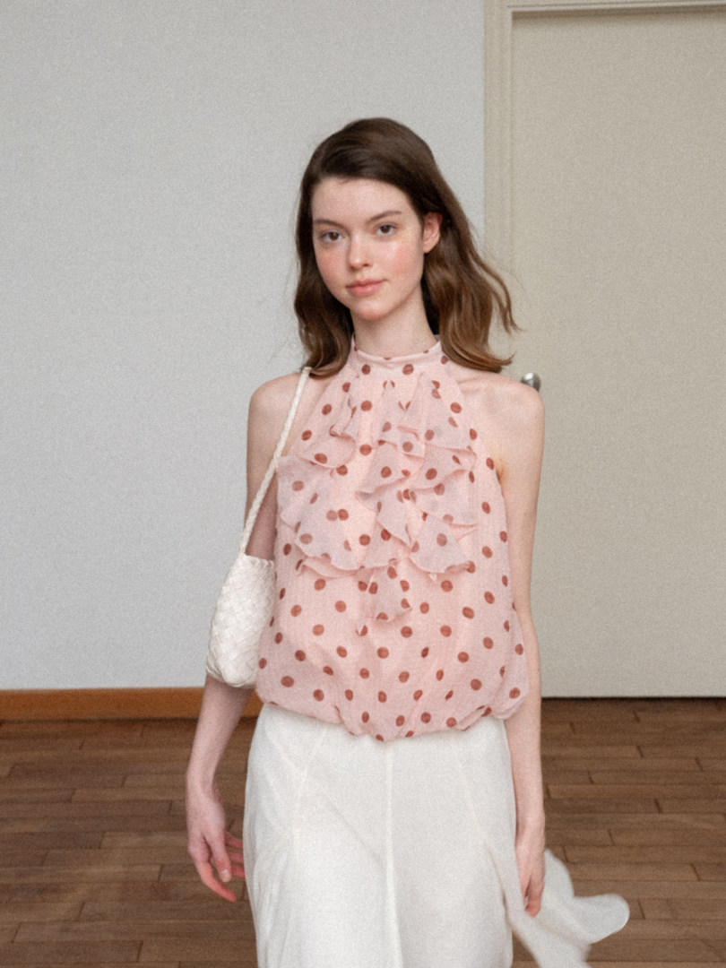 Model wearing a pink polka dot ruffled sleeveless top with a white skirt