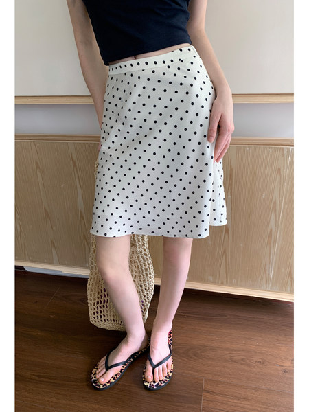 Model wearing a white polka dot skirt with a black top and sandals