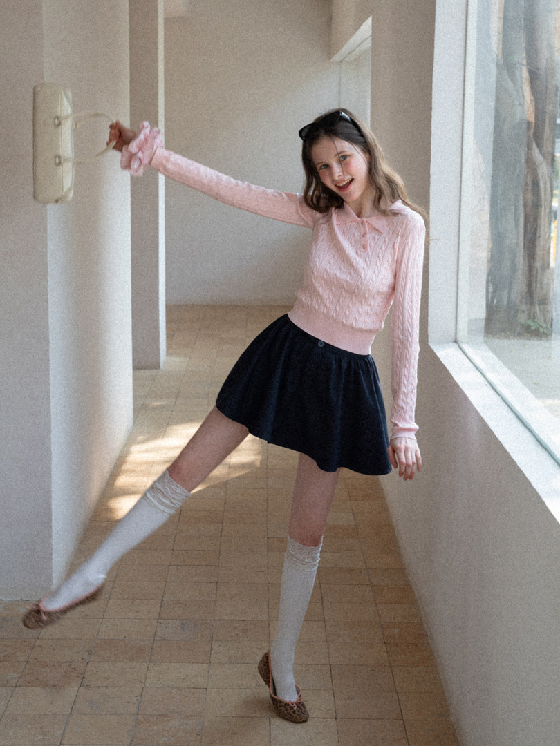 Model wearing a pink knit long-sleeve top with a black skirt and white socks