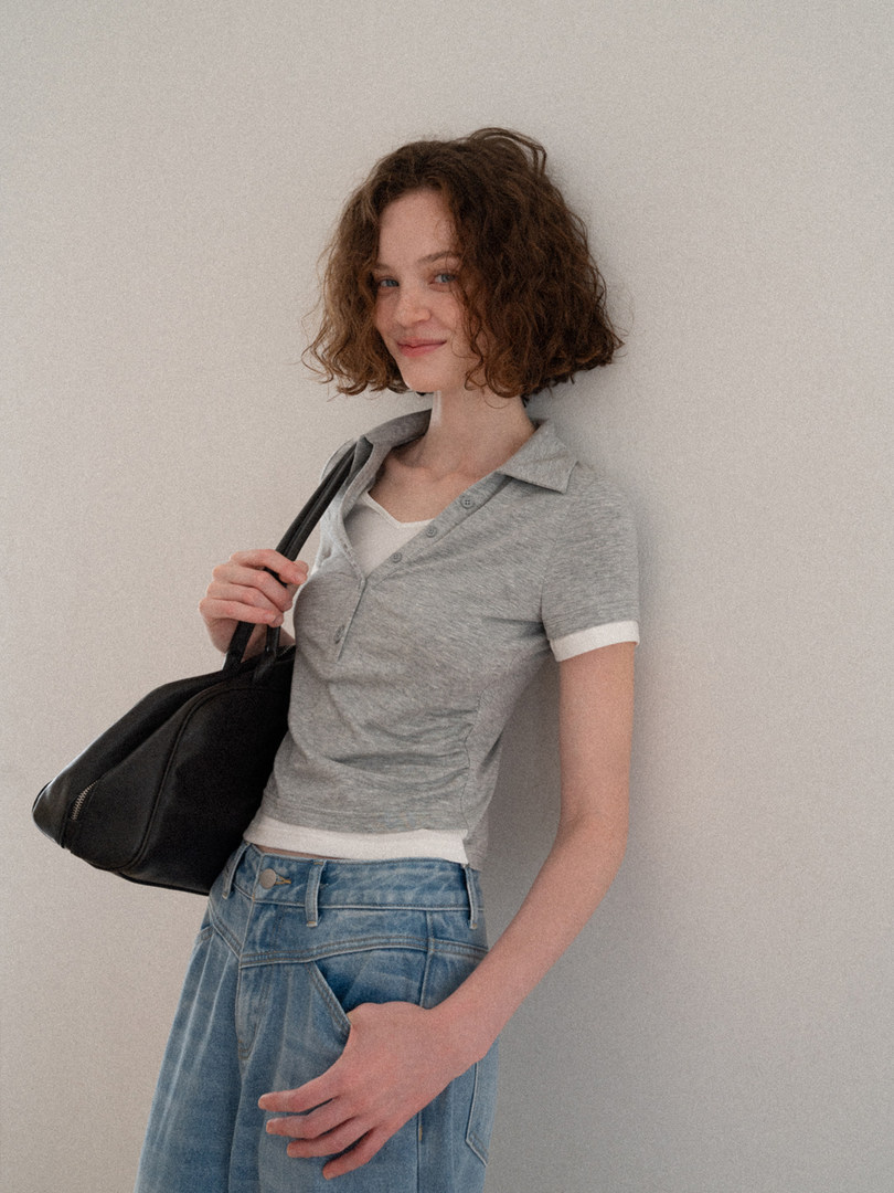 Model wearing a gray short-sleeve polo shirt with blue jeans and a black shoulder bag