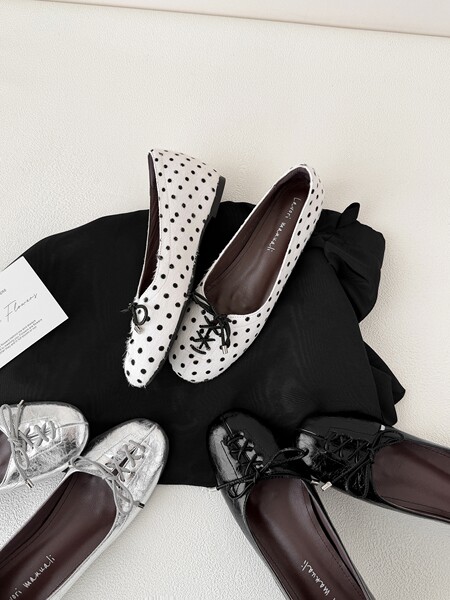 Assorted lace-up flat shoes in polka dot, black, and metallic finishes on a dark fabric backdrop