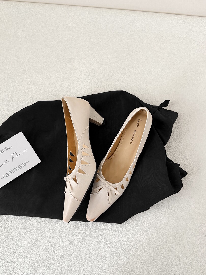 Cream pointed-toe heeled shoes displayed on a black fabric background