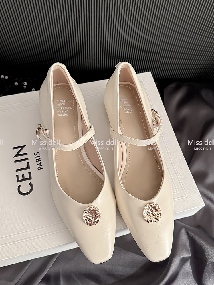 Cream pointed-toe flats with ankle straps and gold embellishments on a box