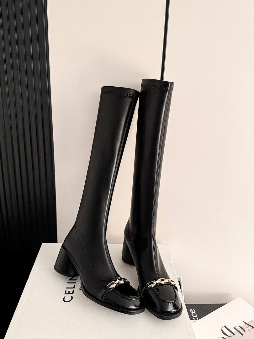 Black knee-high heeled boots with glossy toe caps displayed on a box