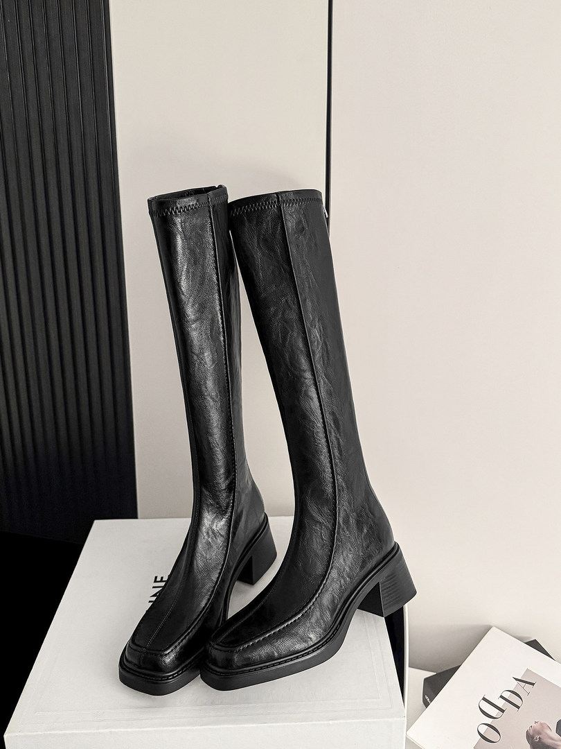 Black leather knee-high boots with block heels on a display box