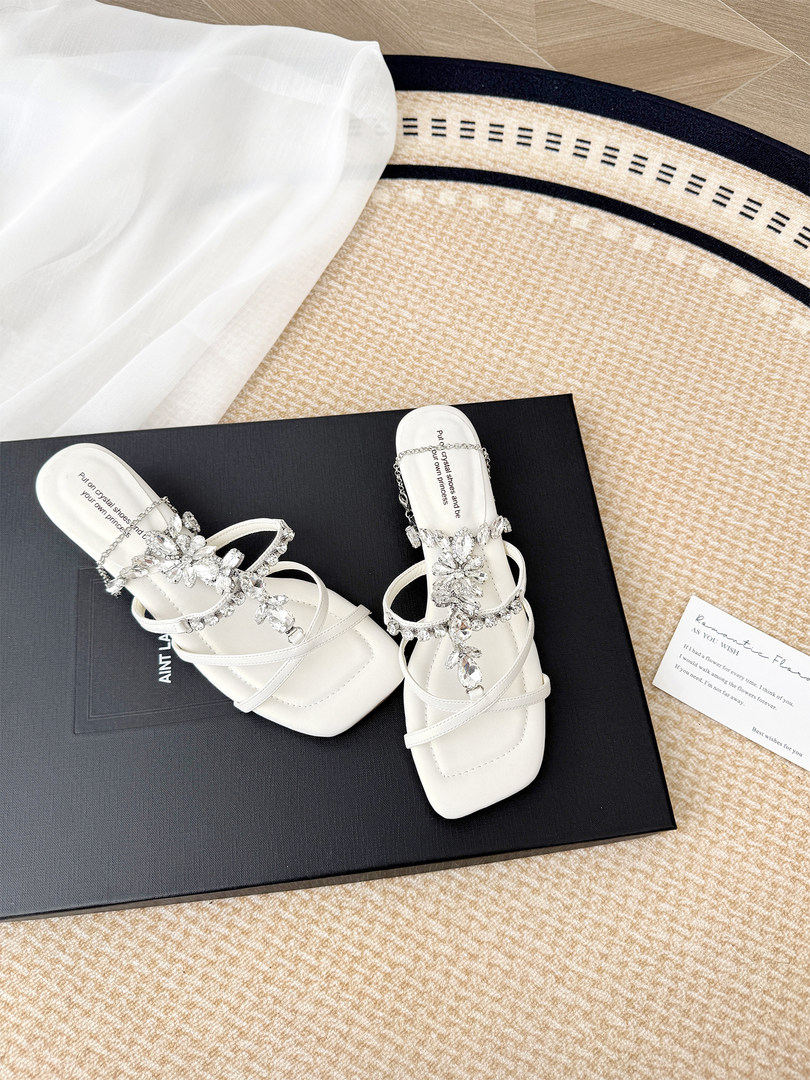 Pair of white embellished heeled sandals displayed on a black box
