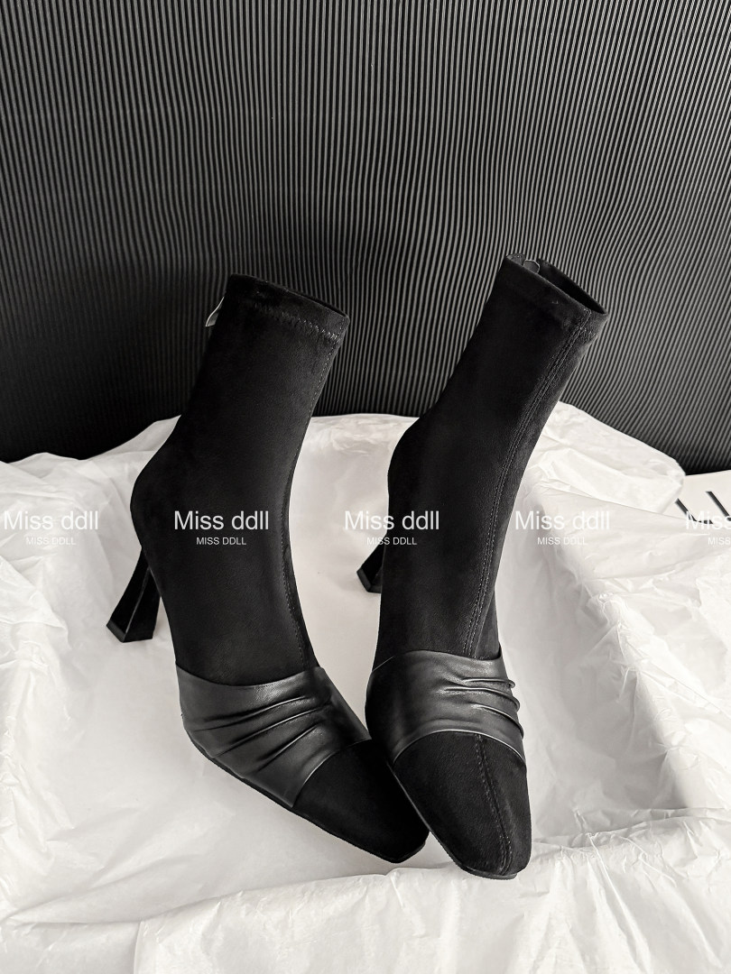 Black knee-high heeled boots displayed on white bedding