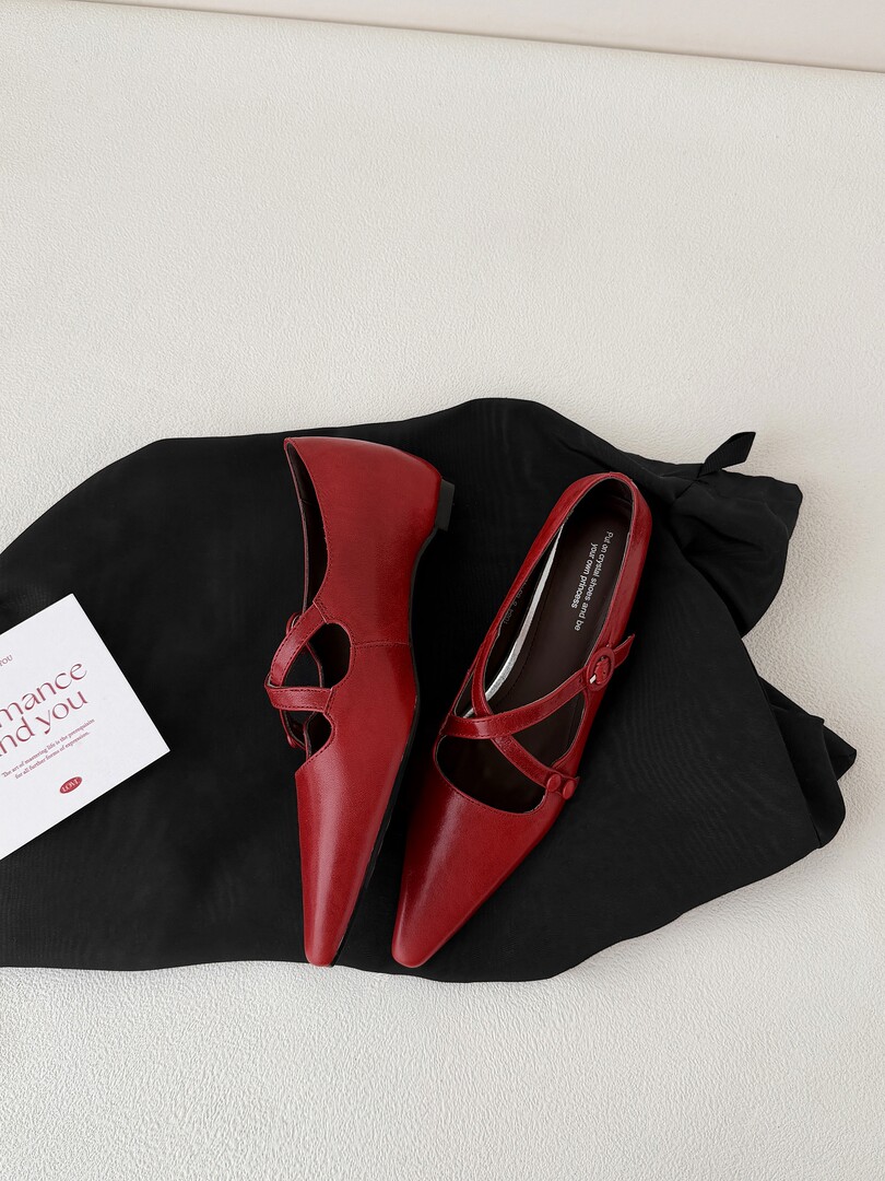Red pointed-toe Mary Jane shoes laid on black fabric