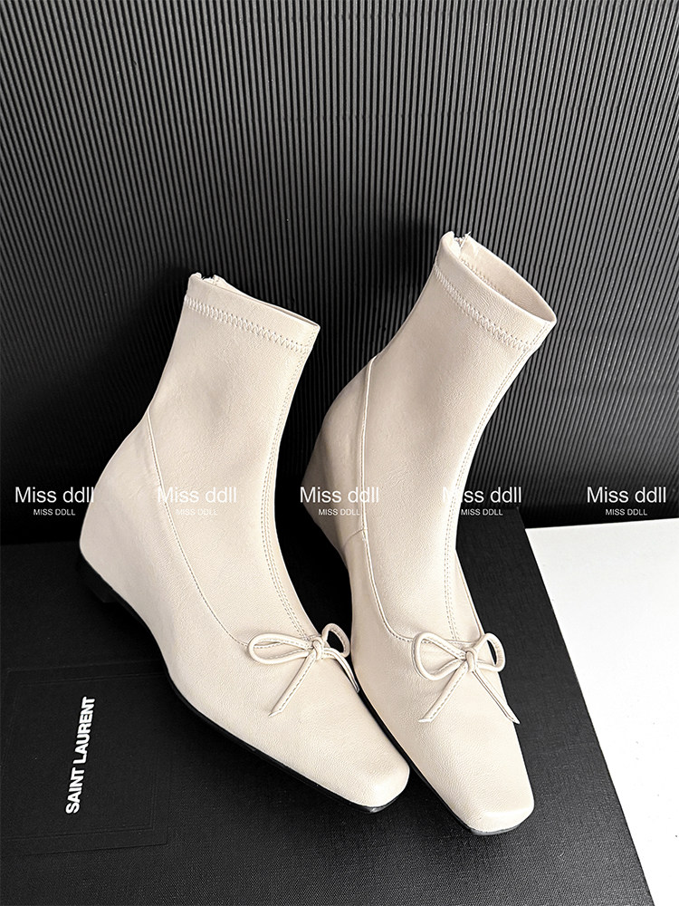 Beige pointed-toe ankle boots with bow detail on display