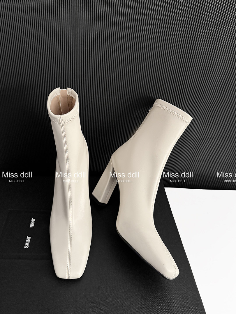 Cream ankle boots with pointed toes and block heels on a black display background