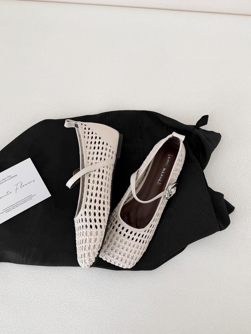 Pair of cream woven flat shoes displayed on a black cloth background