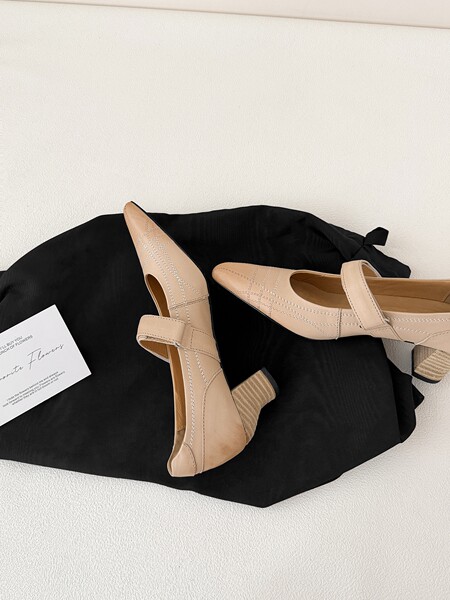 Beige pointed-toe heeled slingback shoes laid on a black bag