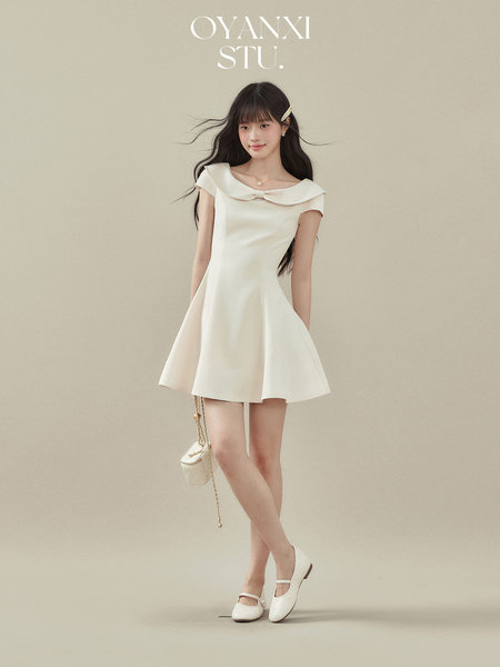 Model wearing a white off-shoulder flared mini dress with a small shoulder bag and flats