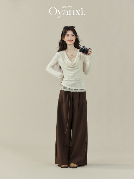 Model wearing a cream draped top with wide brown pants on a studio background