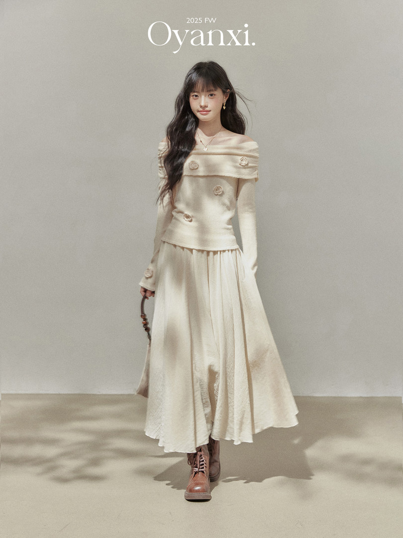 Model wearing a cream off-shoulder knit top and flowing skirt with brown lace-up boots