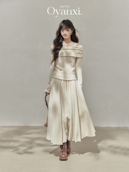Model wearing a cream off-shoulder knit top and flowing skirt with brown lace-up boots