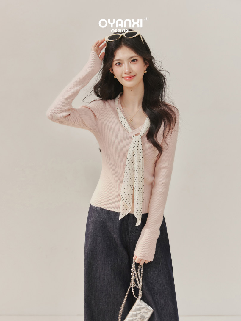 Model wearing a light pink ribbed long-sleeve knit top with a polka dot scarf tie