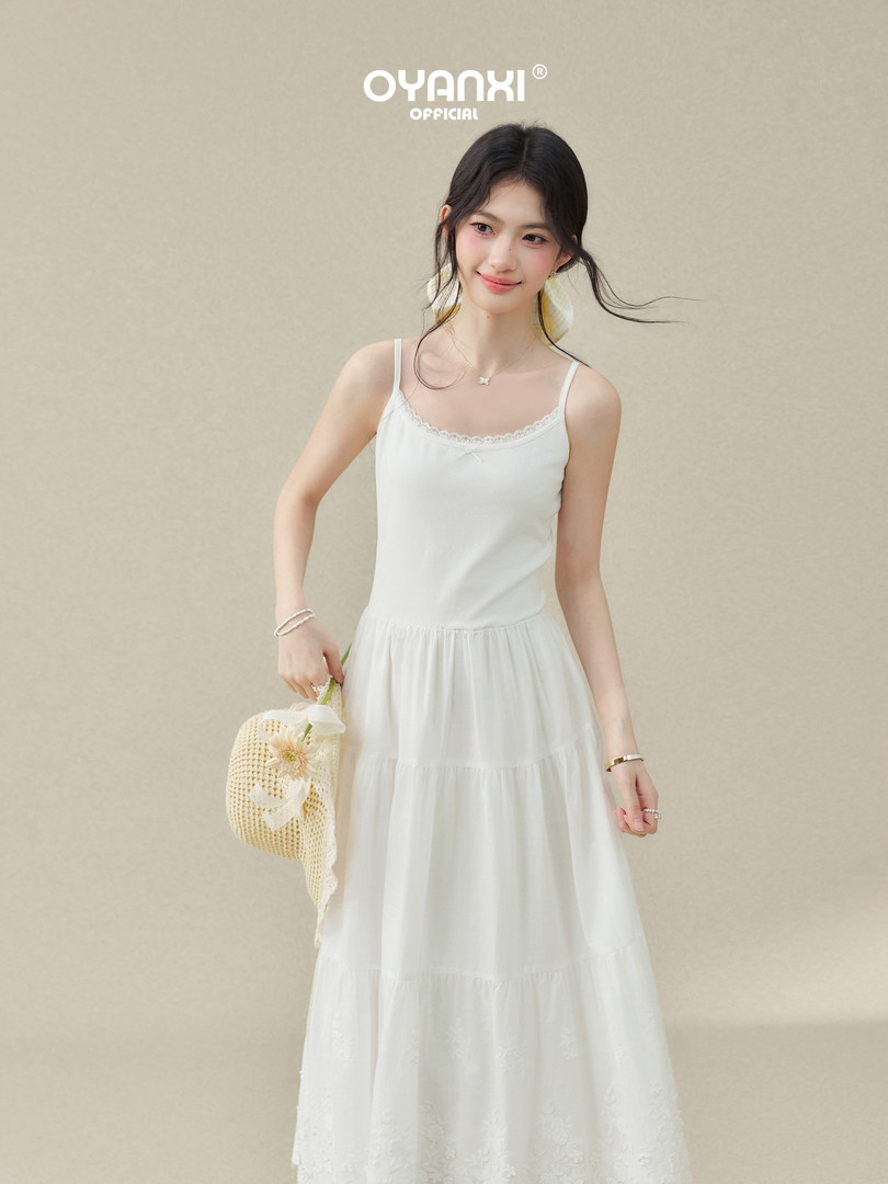 Woman wearing a white spaghetti-strap maxi dress holding a woven bag