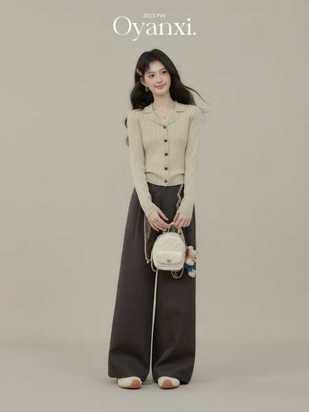 Model wearing a cream knit button-up top with wide dark pants and a small white bag