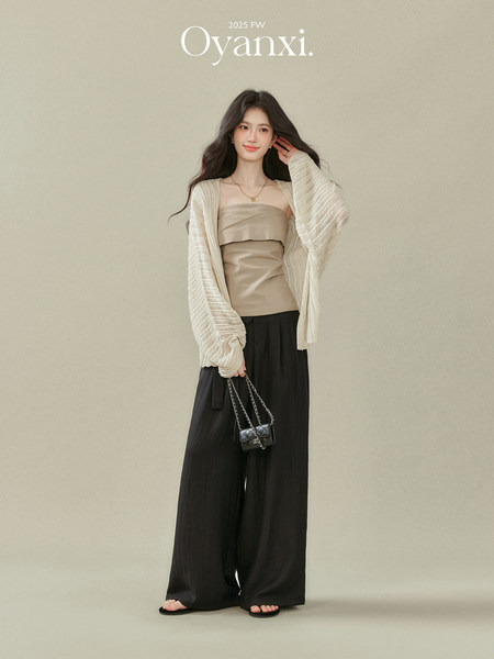 Fashion model wearing a beige strapless top, cream cardigan, black wide-leg pants, and a small black chain bag