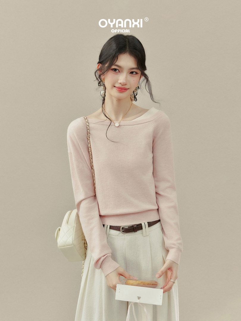 Model wearing a light pink long-sleeve sweater with a cream skirt and small handbag