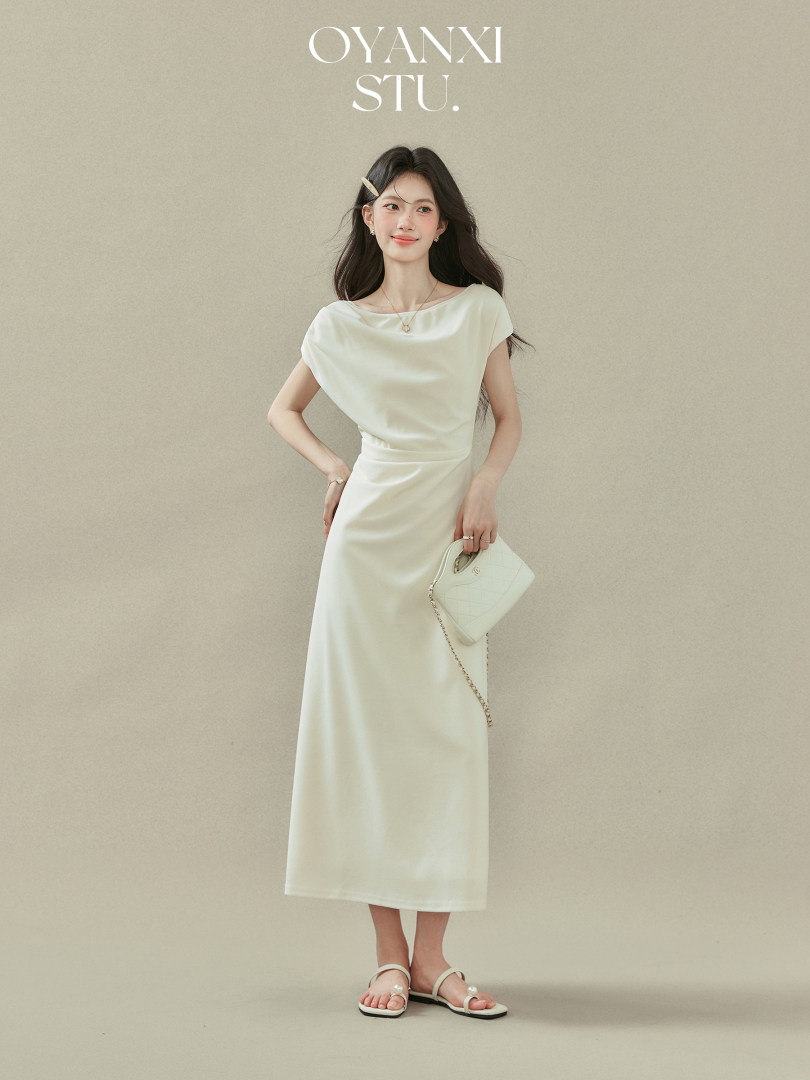 Model wearing a cream sleeveless midi dress with a small white handbag and sandals