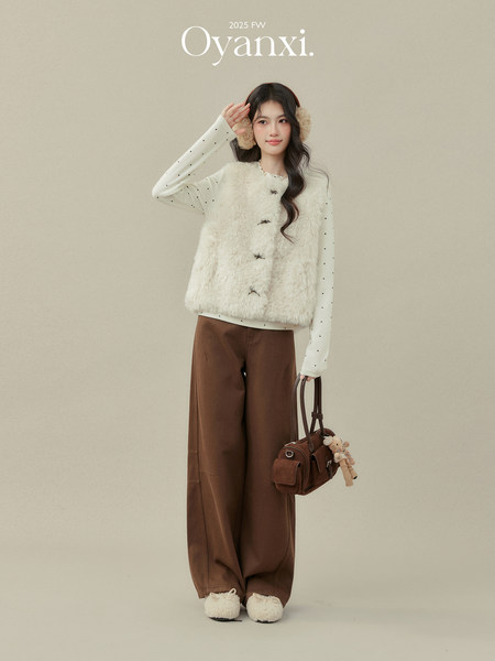 Fashion model wearing a white faux-fur vest, polka dot top, brown wide-leg pants, and a brown handbag