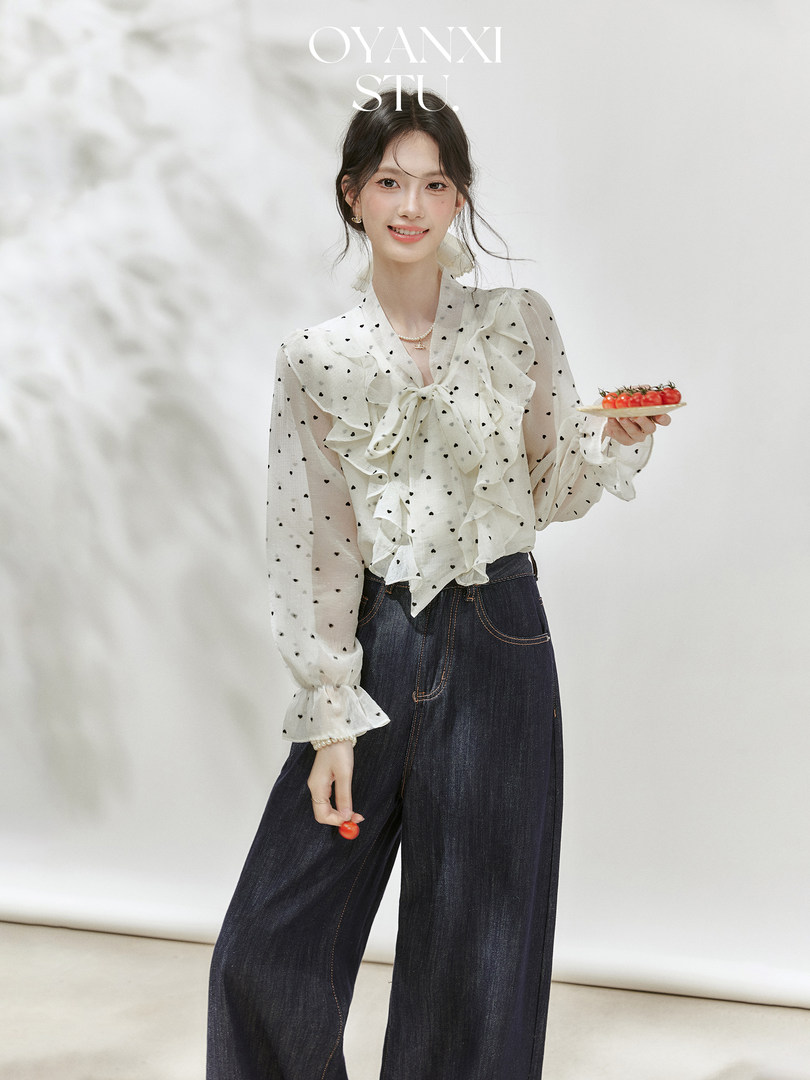 Model wearing a white ruffled polka dot blouse with dark wide-leg jeans