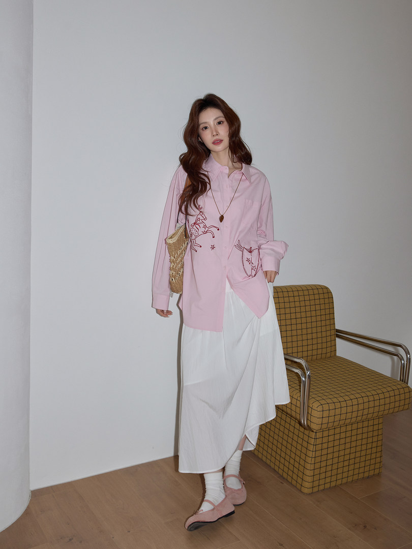 Model wearing a pink oversized graphic shirt with a white skirt and pink flats