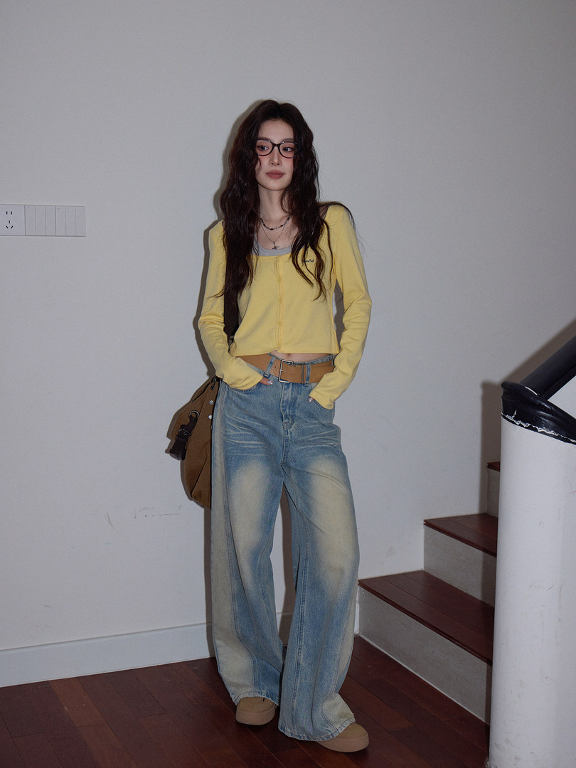 Model wearing a yellow cropped long-sleeve top with loose blue jeans and a brown bag