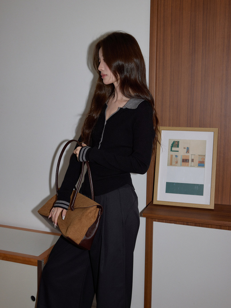 Woman wearing a black top and wide-leg pants while holding a two-tone handbag