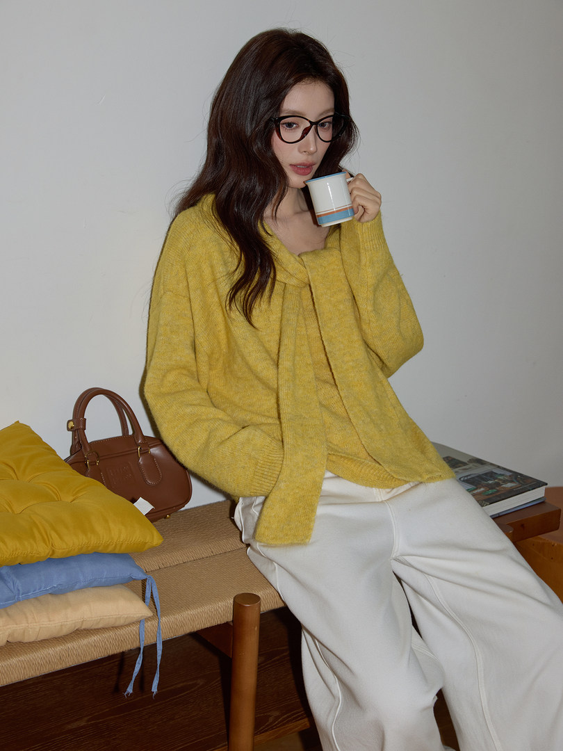 Woman wearing a yellow knit sweater and white trousers seated indoors