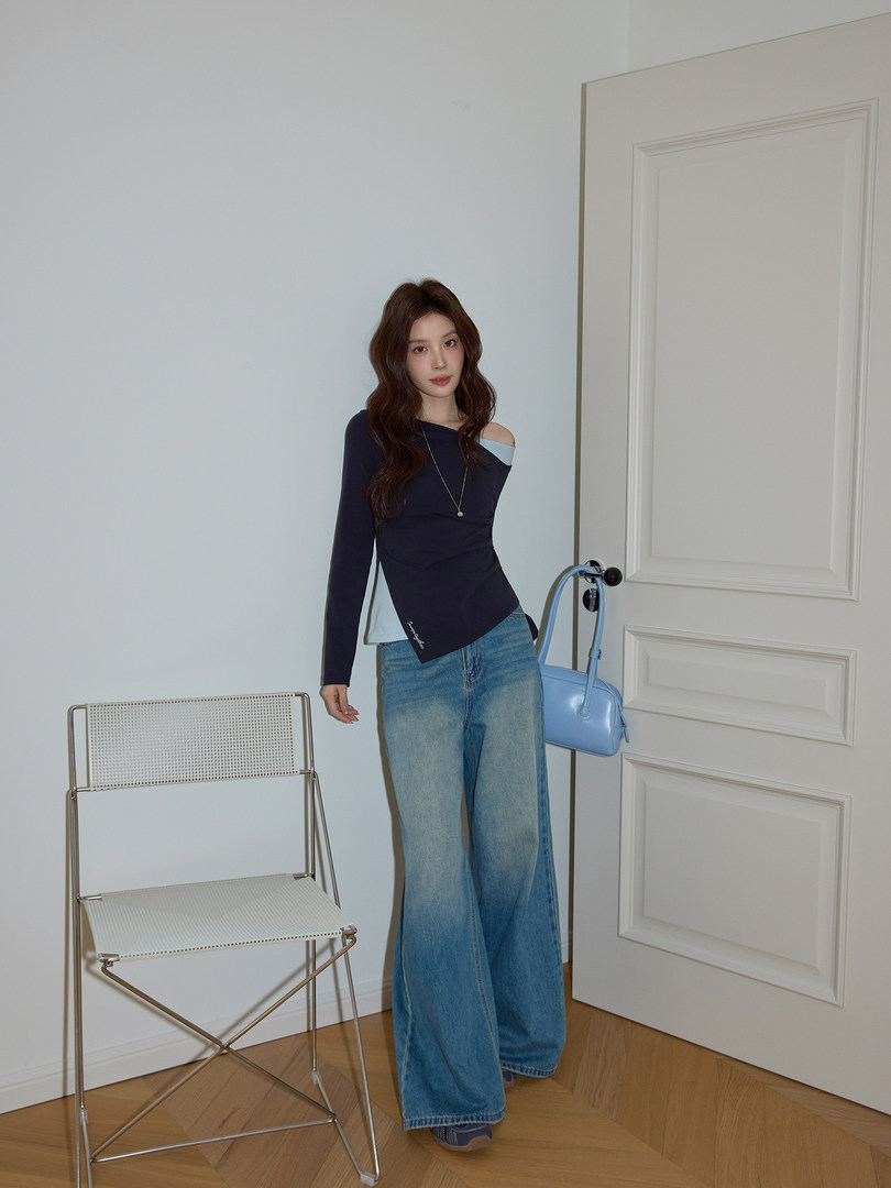 Woman wearing a navy asymmetrical long-sleeve top with wide-leg blue jeans and a light blue handbag