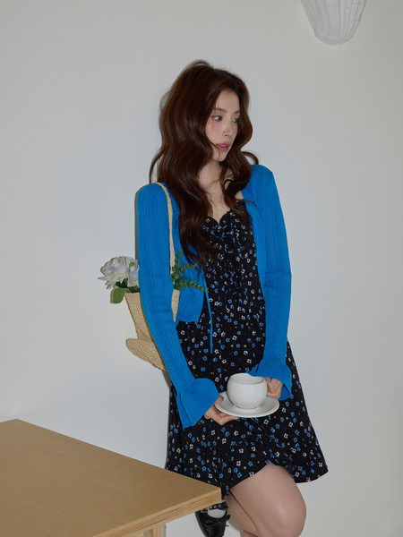 Model wearing a black floral dress with a bright blue cardigan