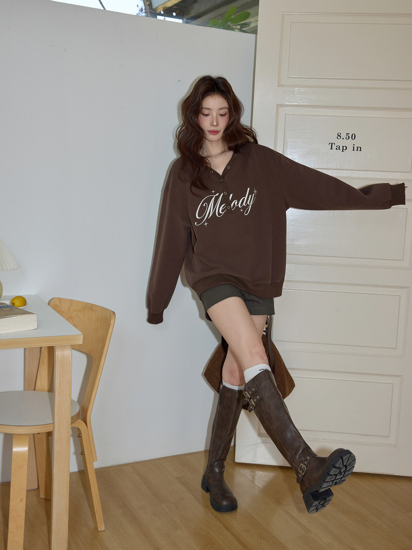 Model wearing a brown oversized sweatshirt with tall brown boots in an indoor setting