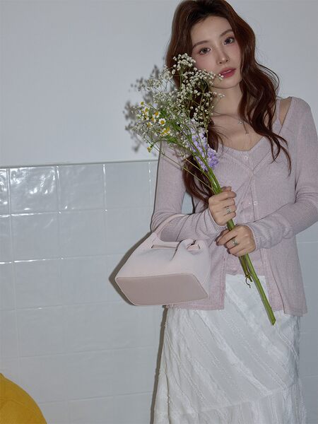 Model wearing a pastel pink cardigan with a white skirt and matching handbag
