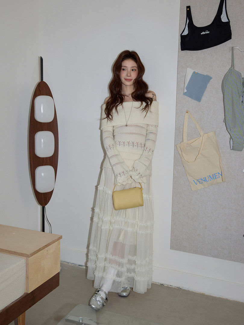 Model wearing an off-shoulder cream knit dress with a sheer layered skirt and yellow handbag