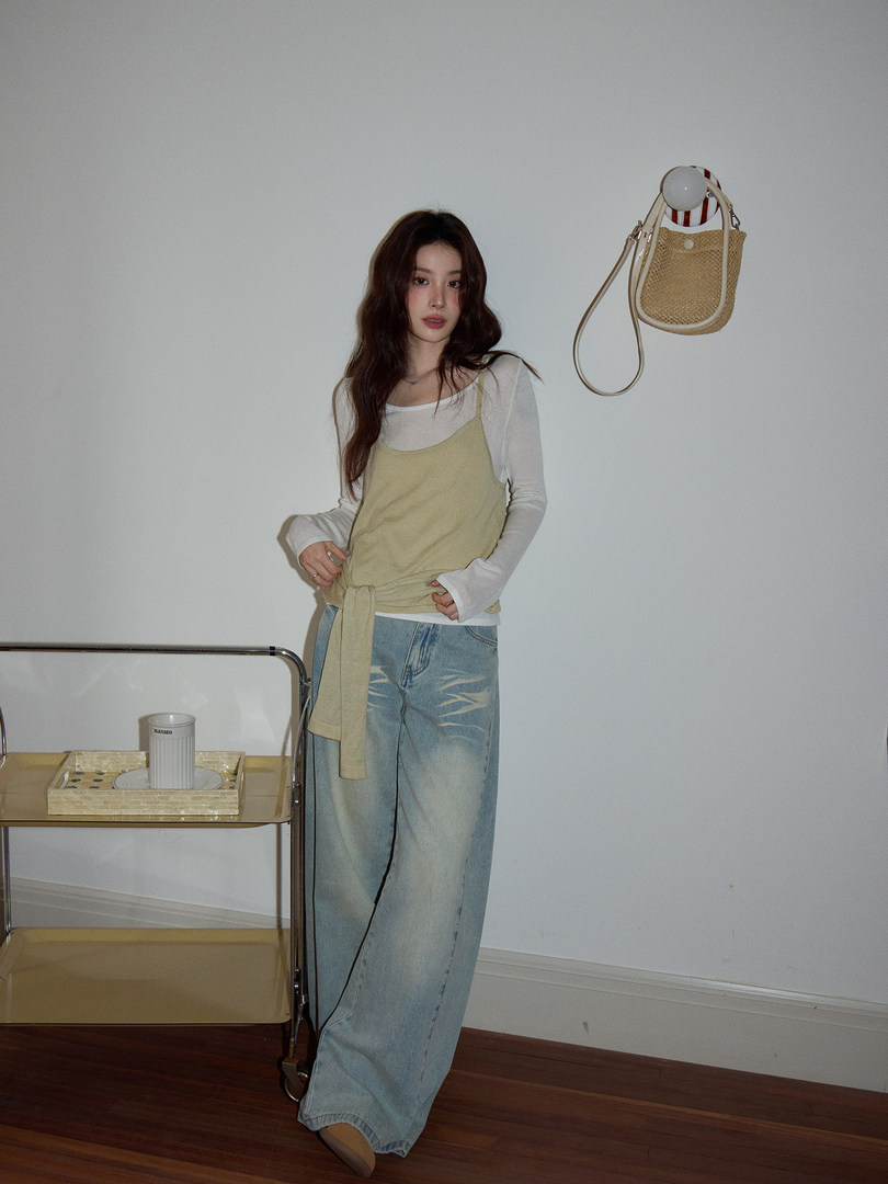 Woman wearing a layered casual outfit with wide-leg jeans and a woven shoulder bag