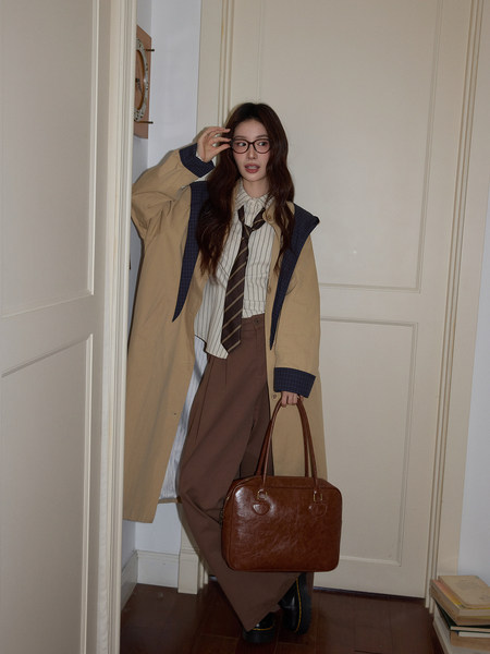 Model wearing a beige trench coat, striped shirt, tie, brown trousers, and carrying a brown leather handbag