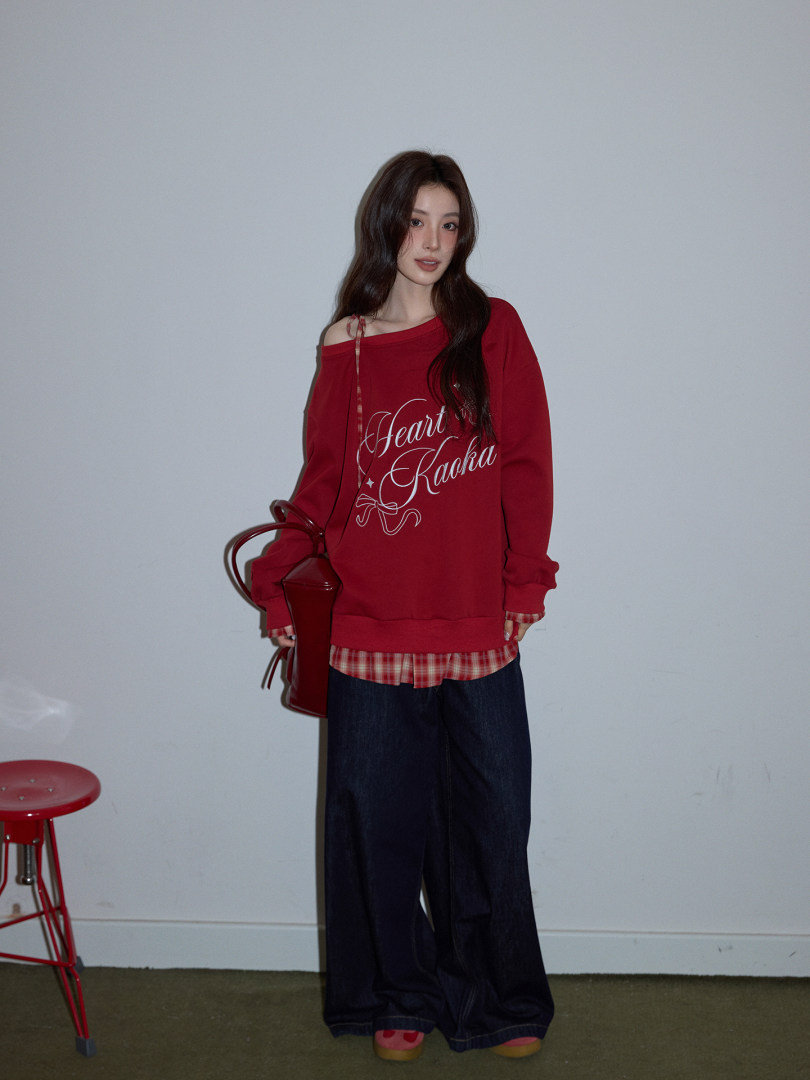 Model wearing a red oversized graphic sweatshirt layered over a plaid shirt with wide-leg jeans