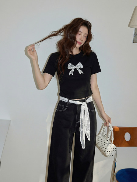 Model wearing a black short-sleeve bow top with wide-leg pants and lace belt detail