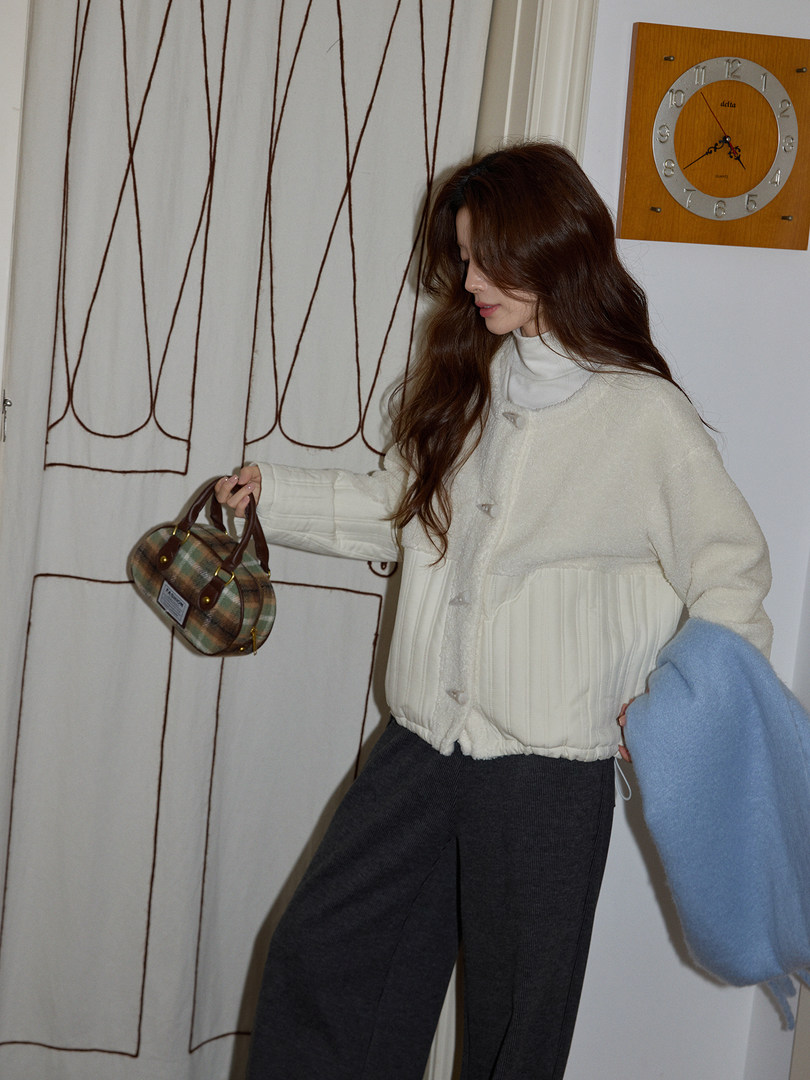 Model wearing a cream textured jacket with dark pants and a small handbag
